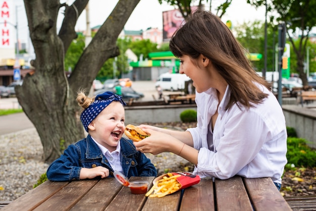 Bastante joven madre e hija comiendo una gran hamburguesa en un café