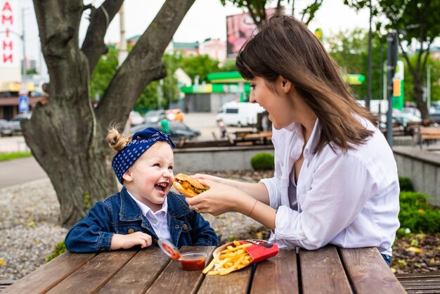 Bastante joven madre e hija comiendo una gran hamburguesa en un café