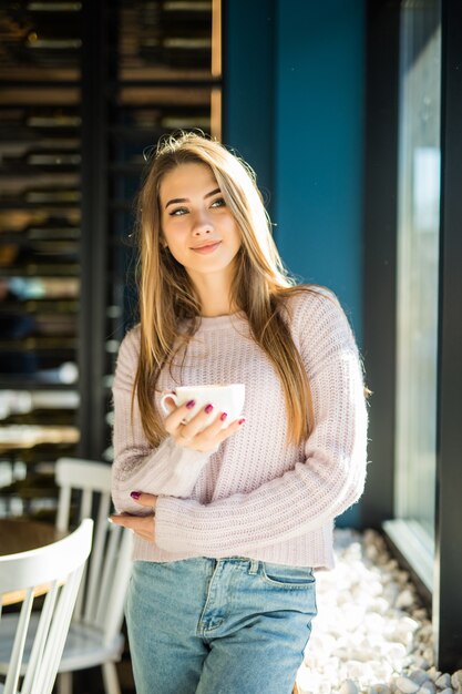 Bastante joven modelo adolescente vestida con ropa casual jeans en café tiene taza de té de café en sus manos