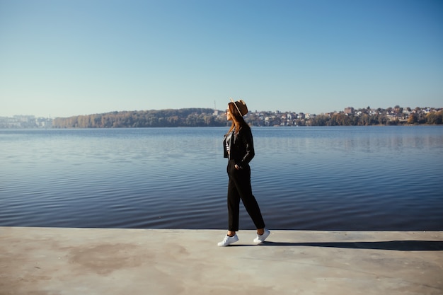 Bastante joven modelo chica mujer posando en día de otoño en la orilla del lago vestida con ropa casual