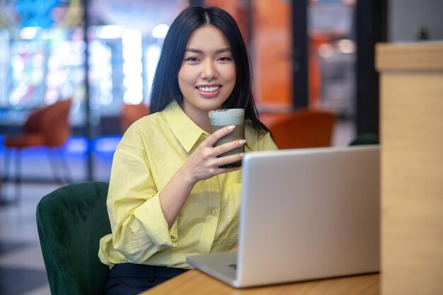 Bastante joven mujer asiática en camisa amarilla trabajando en una computadora portátil