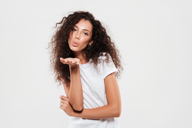 Foto gratuita bastante joven mujer con cabello rizado enviando beso de aire