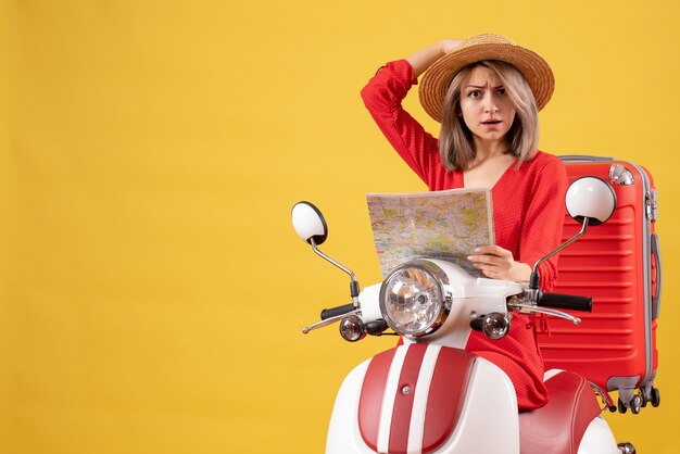 Bastante joven mujer en ciclomotor con maleta roja sosteniendo el mapa