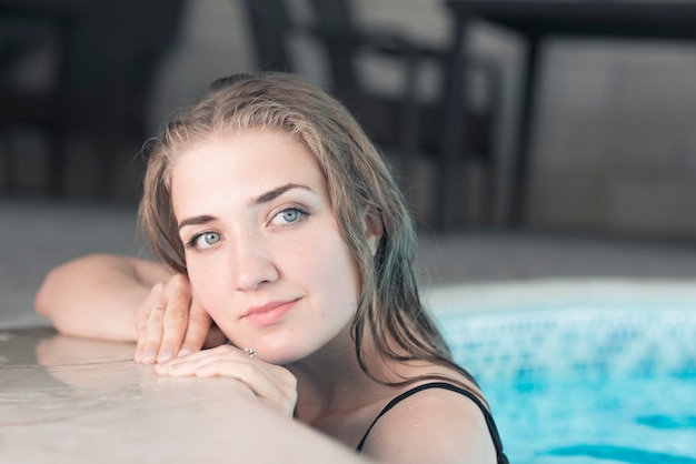 Bastante joven mujer inclinada en el borde de la piscina