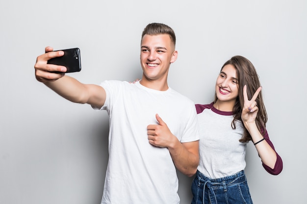 Bastante joven pareja guapo chico y chica haciendo selfie en su teléfono aislado en blanco