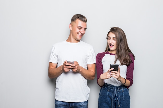 Bastante joven pareja guapo chico y chica mirando el uno al otro teléfono aislado en blanco