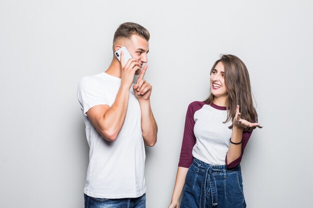 Bastante joven pareja guapo tiene una conversación secreta en pnone cerca de su chica aislada en blanco