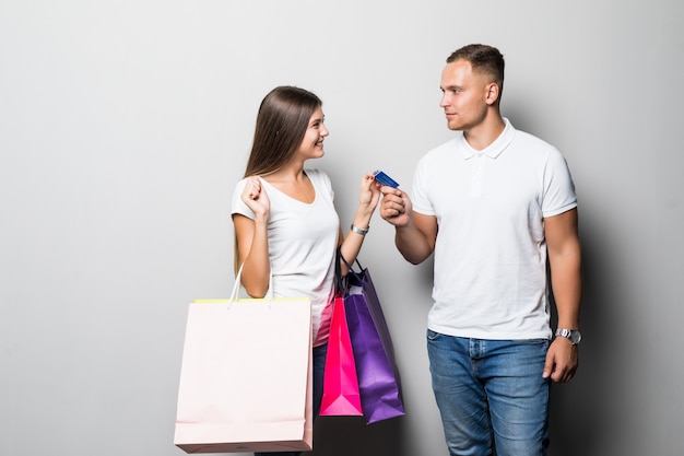 Foto gratuita bastante joven pareja sonriente estudiante soleado sosteniendo un montón de bolsas de colores aisladas sobre fondo blanco.