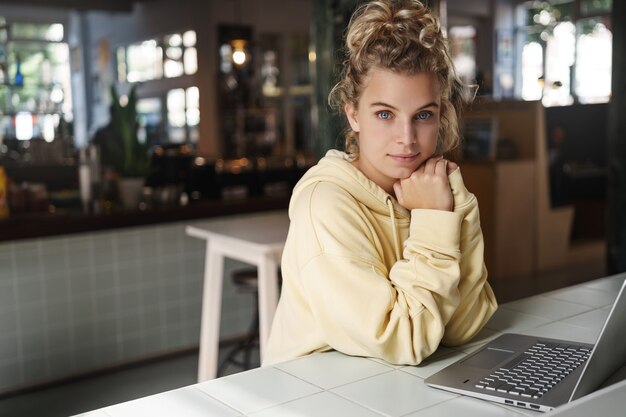 Bastante joven se sienta sola en un café con una computadora portátil.