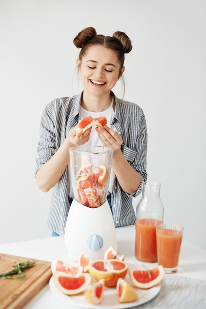 Bastante joven sonriente mezcla de desintoxicación refrescante batido de pomelo sobre pared blanca. concepto de comida saludable.