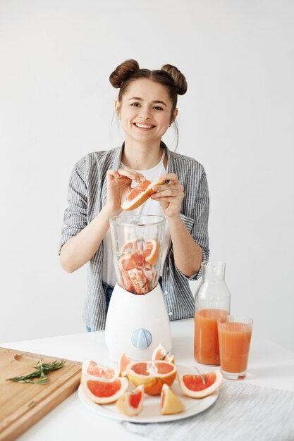 Bastante joven sonriente mezcla de desintoxicación refrescante batido de pomelo sobre pared blanca. Concepto de comida saludable.