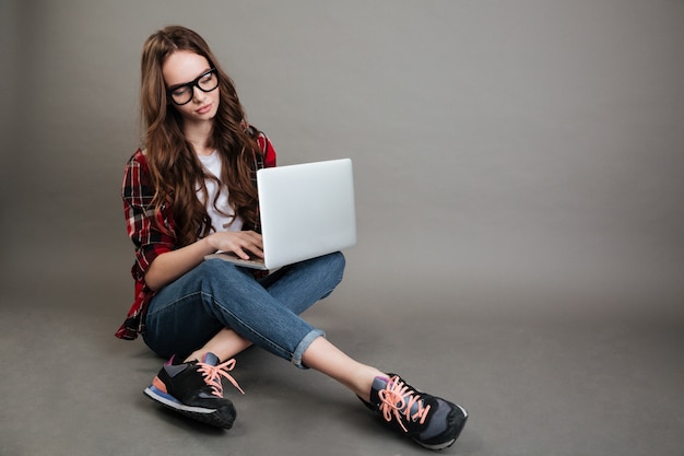 Bastante jovencita chateando por computadora portátil. Mirando a un lado