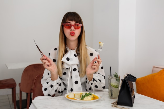 Foto gratuita bastante linda mujer disfrutando de su desayuno saludable en la cafetería moderna y elegante