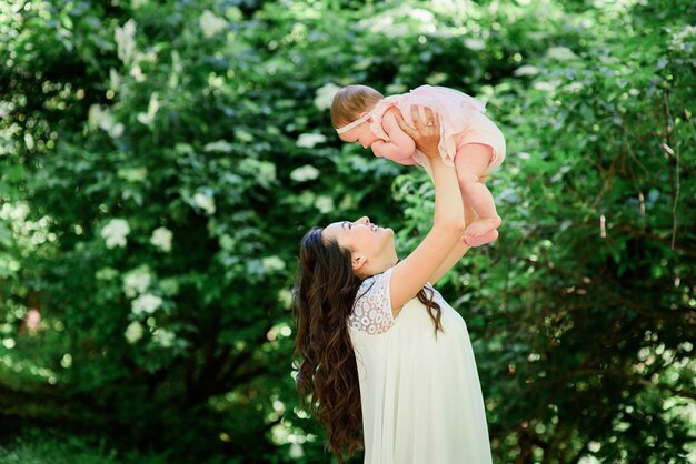 Bastante morena mujer en vestido blanco plantea con su pequeña hija en el jardín