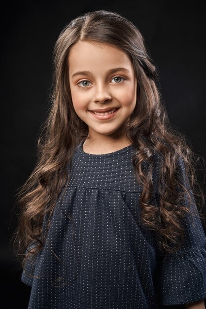 Bastante pequeña modelo en hermoso vestido gris posando, sonriendo.