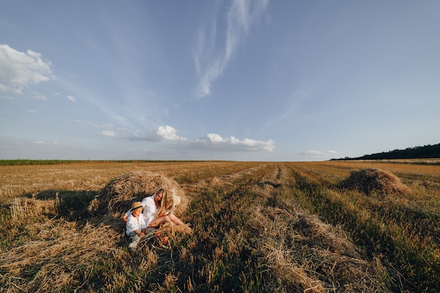 Bastante rubia mujer de pelo largo con pequeño hijo rubio al atardecer relajarse en el campo y saborear la fruta de una cesta de paja. verano, agricultura, naturaleza y aire fresco en el campo.