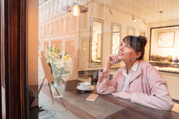 Bastante soñando mujer joven sentada en la mesa de café