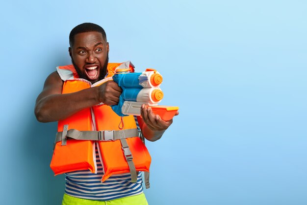 Batalla de lucha acuática. Hombre negro emocional grita que te dispararé, sostiene una pistola de agua de juguete