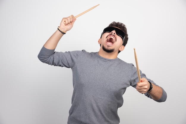 Un baterista con gafas de sol negras sosteniendo baquetas y se ve muy enérgico.