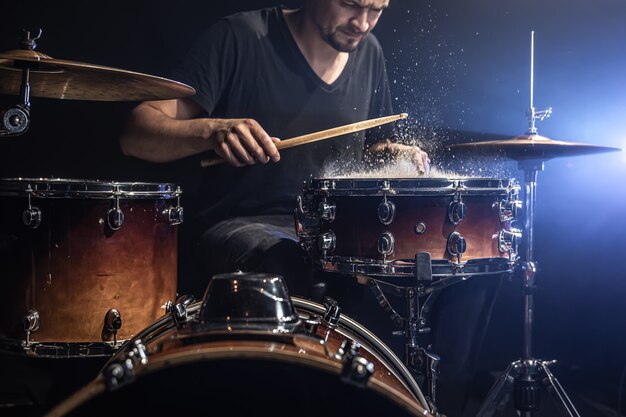 Un baterista masculino toca baquetas en un tambor con salpicaduras de agua en una habitación oscura.