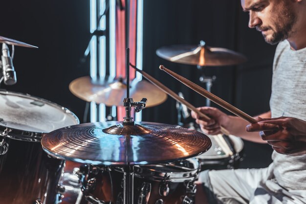 Un baterista masculino tocando la batería en una habitación oscura con una hermosa iluminación.