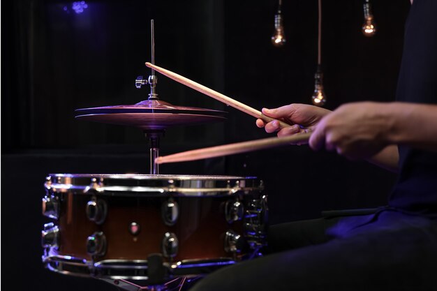 El baterista tocando baquetas en un tambor en la oscuridad. Concepto de concierto y actuación en directo.