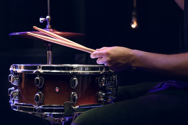 El baterista tocando baquetas en un tambor en la oscuridad. Concepto de concierto y actuación en directo.