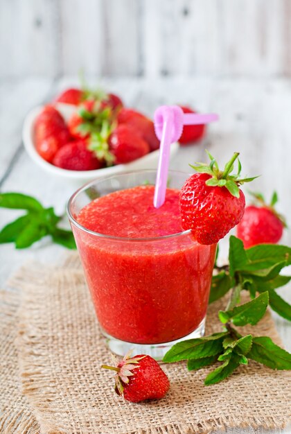 Batido de fresa en vidrio y hojas de menta en una mesa de madera en estilo rústico