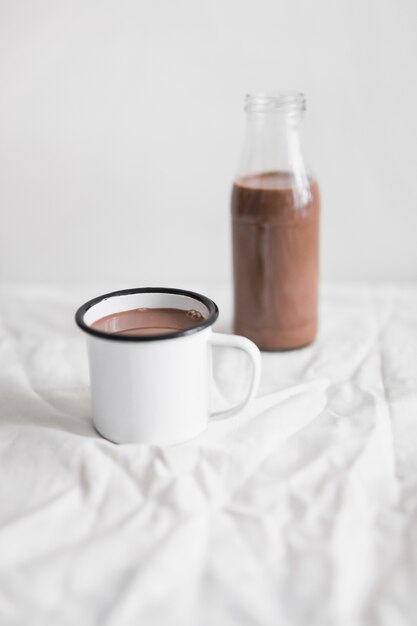 Batido de leche con chocolate en la taza blanca y botella de vidrio en la mesa con tela blanca