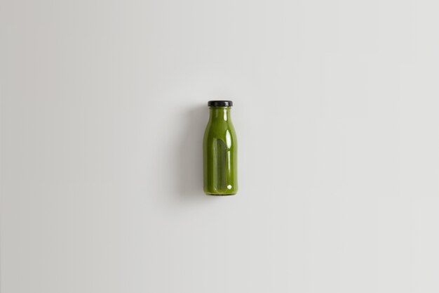 Batido de vegetales verdes saludable preparado a base de espinacas, col rizada y pepinos mezclados con agua para una nutrición adecuada. Botella de bebida nutritiva de ingredientes orgánicos sobre fondo blanco.