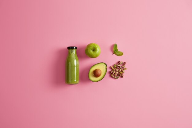 Batido verde saludable hecho de jugosa manzana, aguacate, pistacho y menta. Fondo rosado. Bebida nutritiva fresca para una dieta equilibrada. Ingredientes para preparar bebida nutritiva refrescante.