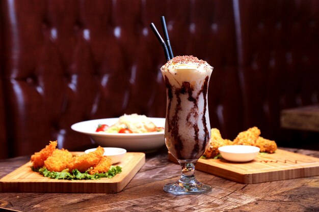 Batido de vista frontal con crema batida y glaseado de chocolate con aperitivos y ensalada en la mesa