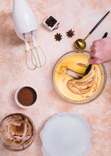 Batidora eléctrica; polvo de cacao; Anís y una persona mezclando la masa del pastel con una espátula.