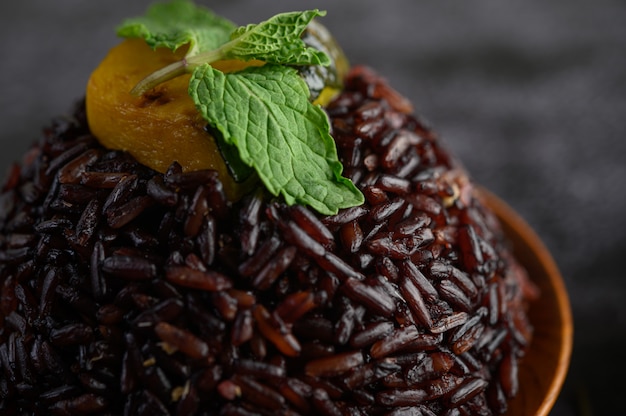 Bayas de arroz morado cocinado en un plato de madera con hojas de menta y calabaza.