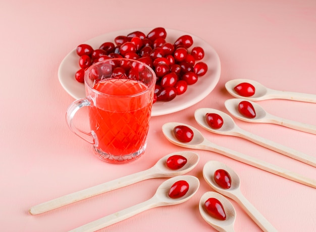 Bayas de cornejo con bebida en plato y cucharas de madera en rosa, vista de ángulo alto.