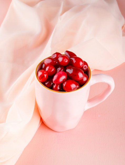 Bayas de cornejo en una taza de vista de ángulo alto en rosa y textil