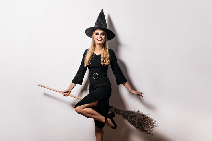 Photo Gratis beautiful female model in carnival costume laughing on white wall. blissful witch posing with broom at halloween party.