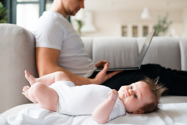 Bebé acostado en la manta cerca de padre usando laptop