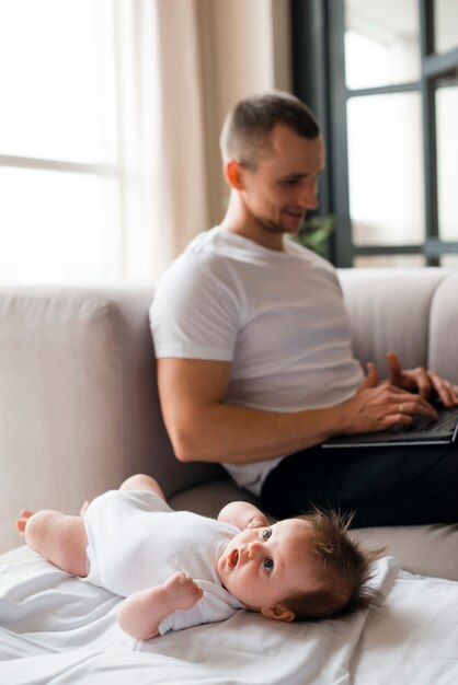 Bebé acostado en la manta cerca de padre usando laptop