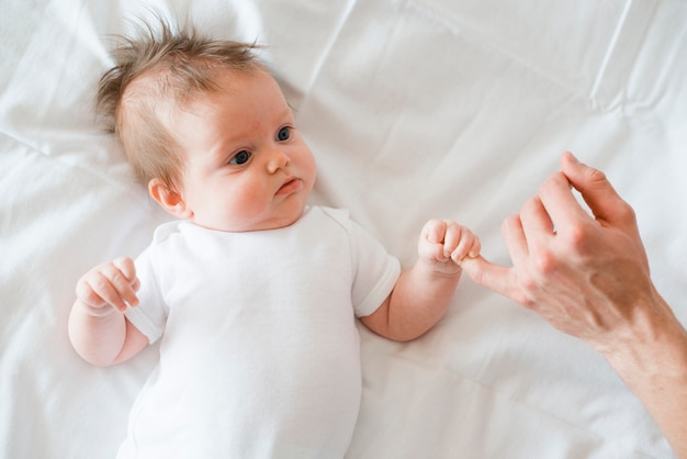 Bebé acostado y sosteniendo el dedo meñique del padre