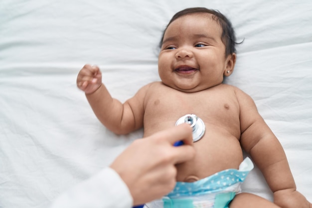 Bebé afroamericano sonriendo confiado teniendo un examen médico en el dormitorio