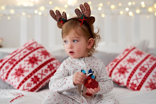 Foto gratuita bebé encantador abriendo el regalo de navidad en la cama