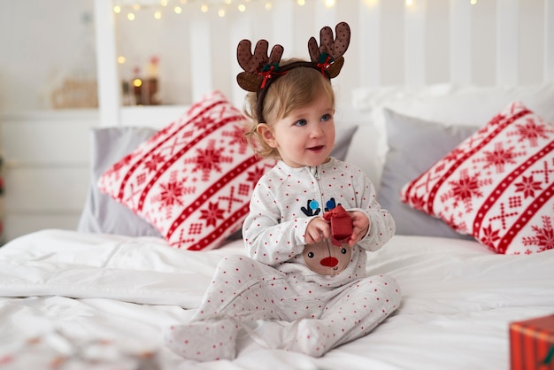 Bebé encantador abriendo el regalo de Navidad en la cama