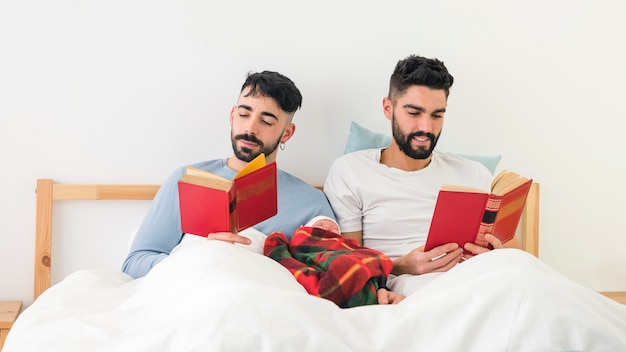 Bebé envuelto en una manta entre la pareja gay leyendo el libro.