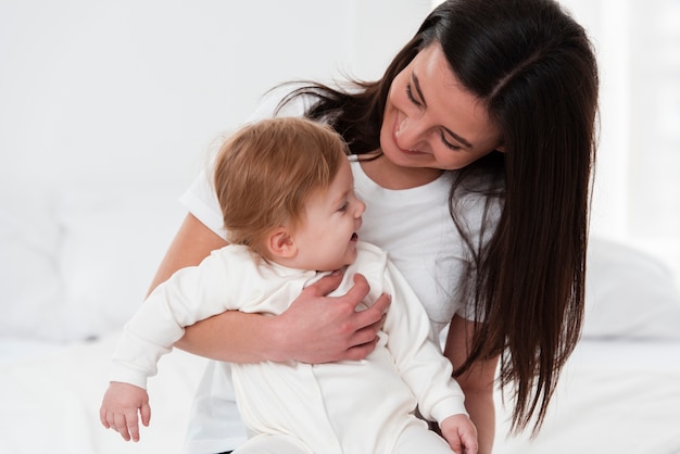 Bebé feliz sostenido por la madre en la cama