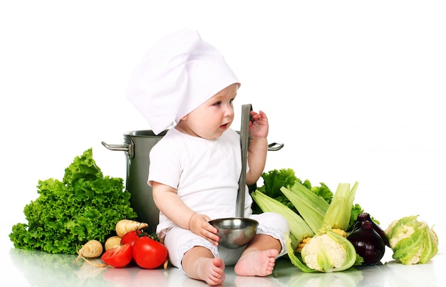 Bebé con gorro de chef rodeado de verduras