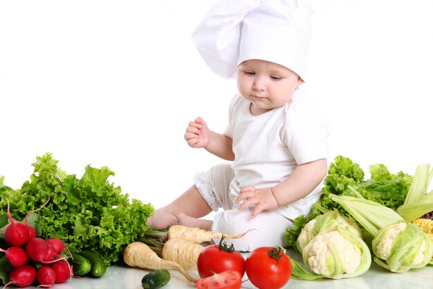 Bebé con gorro de chef rodeado de verduras