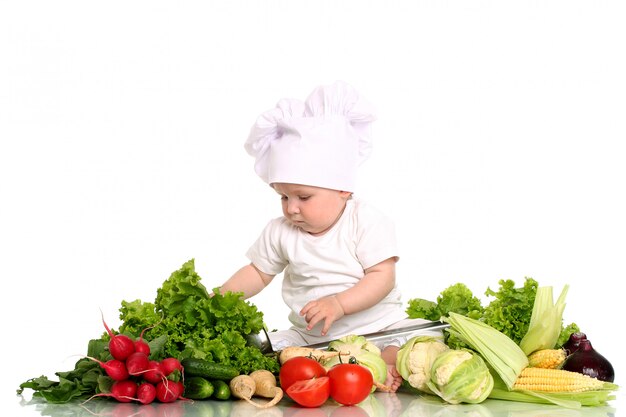 Bebé con gorro de chef rodeado de verduras