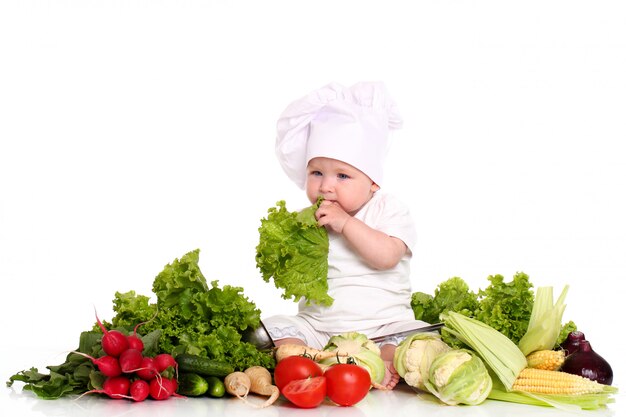Bebé con gorro de chef rodeado de verduras