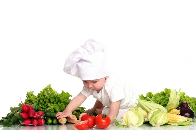 Bebé con gorro de chef rodeado de verduras